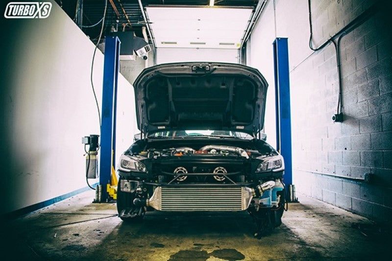 Turbo XS FMIC 2015-2017 Subaru STi - Wrinkle Red Pipes installed in a Subaru STi on a lift with engine hood open.